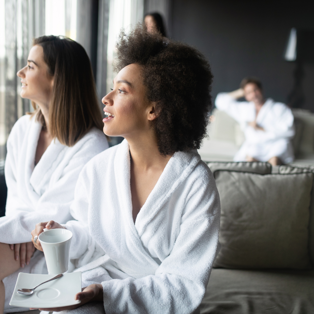 two women looking out the window from a spa lounge, another woman in the background sits on a chair.