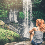 Embodied Adventurer woman sitting on rocks looking at waterfalls (embodied adventurer)