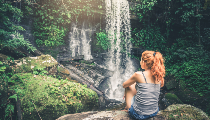 woman sitting on rocks looking at waterfalls (embodied adventurer)