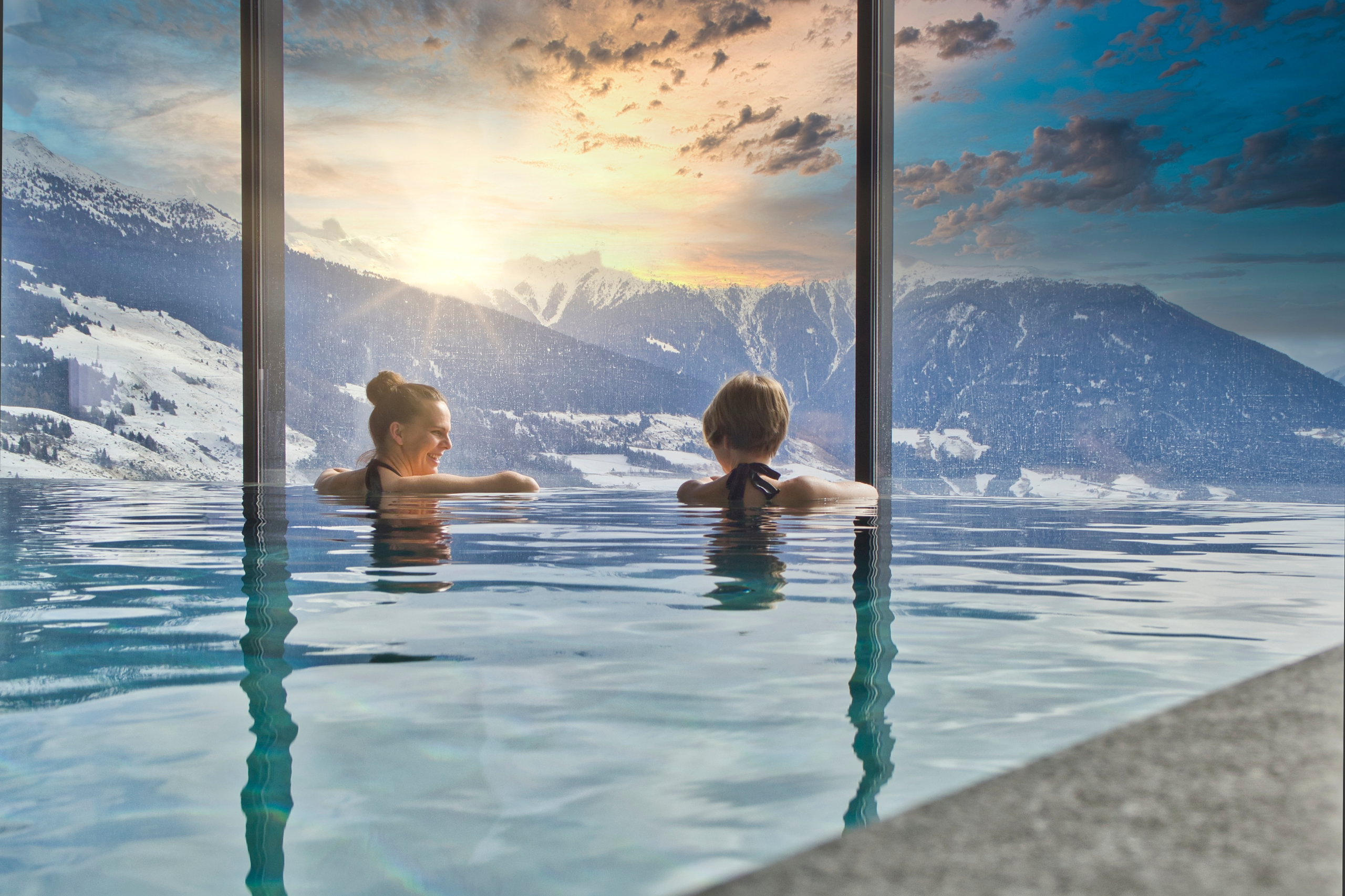 two women in an indoor spa pool looking outdoors at a winter landscape
