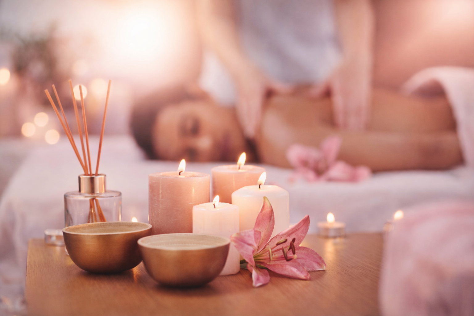 candles in focus with a blurred massage room in background - out of focus woman on a massage table getting a massage